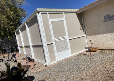 Beige shed beside house with yard decor.