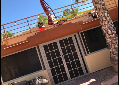 Balcony with workers and red crane beside palm tree.
