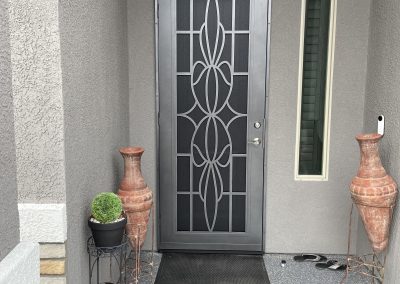 Black front door with decorative glass and planters beside.